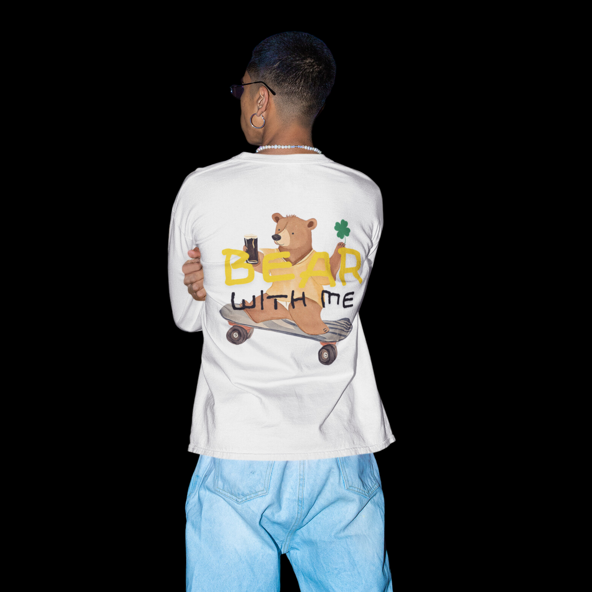 Long sleeve t-shirt featuring a playful graphic on the back of a bear riding a skateboard while holding an Irish beer and a shamrock. The text 'Bear With Me' is displayed above the bear. 