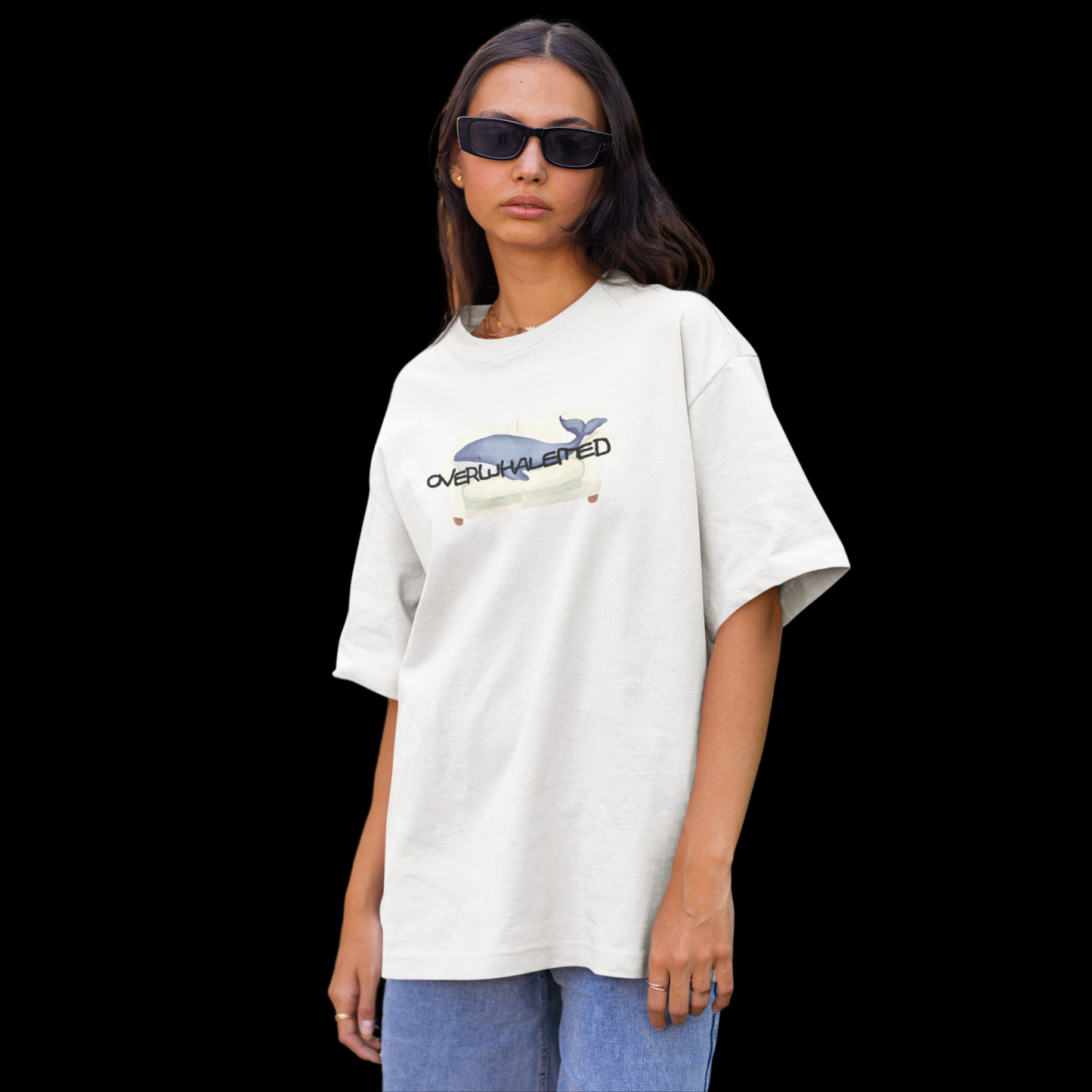 A white t-shirt featuring a playful design of a whale laying on a couch, with the word "Overwhalemed" written above.