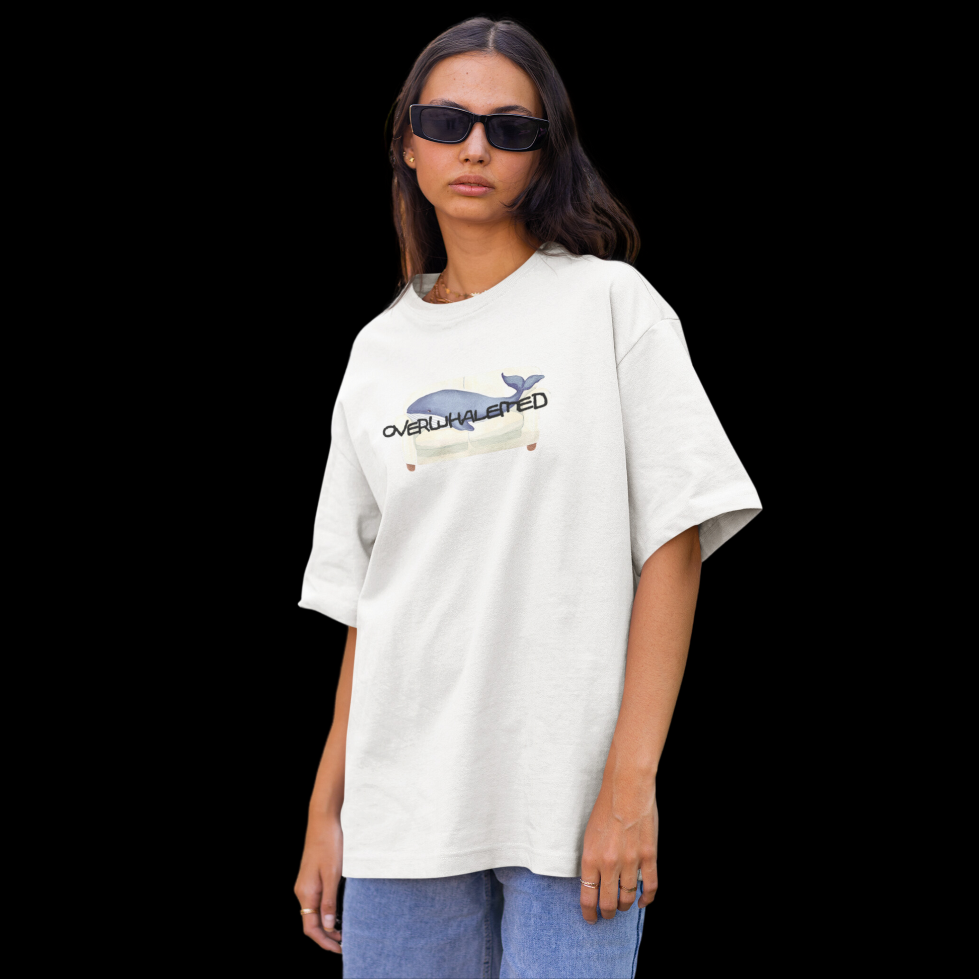 A white t-shirt featuring a playful design of a whale laying on a couch, with the word "Overwhalemed" written above.